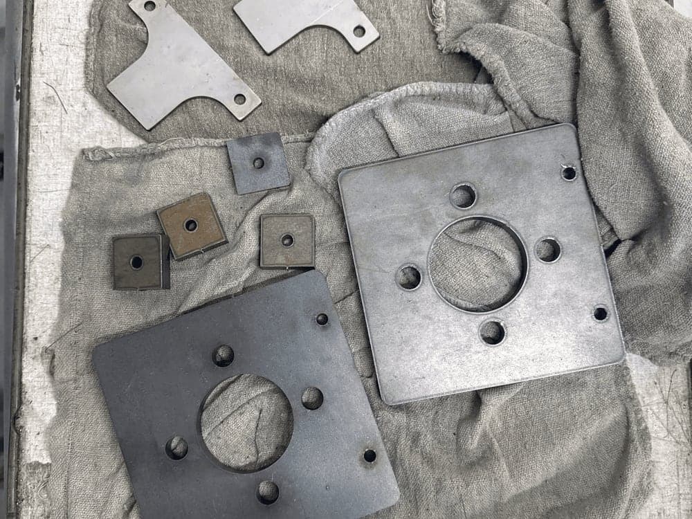 Cut steel plates and brackets laid out on a cloth before welding.