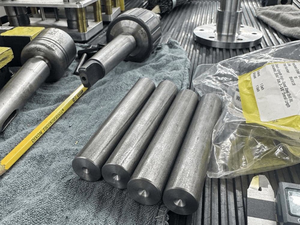 Lengths of steel round bar and tube laid out on a workbench alongside a tape measure.