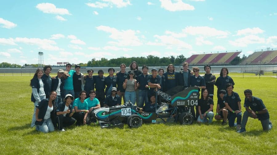 The Gaucho Racing team gathered around the car for a group photo on the grass at competition.
