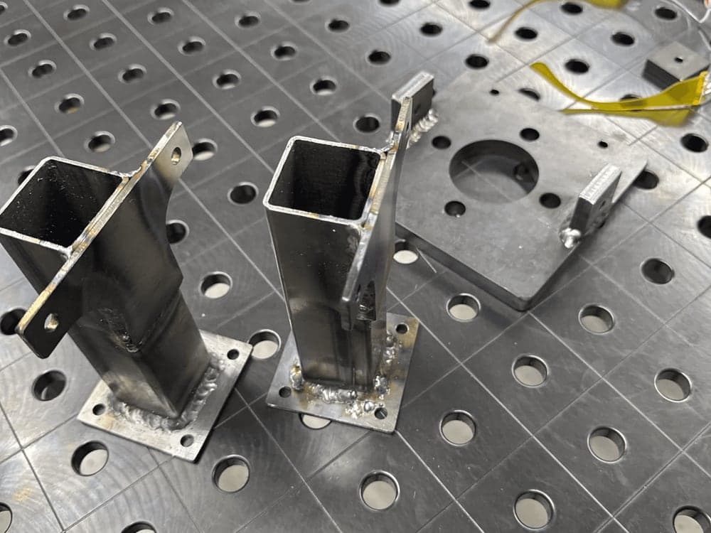 Welded square-tube uprights clamped on a fixture table.